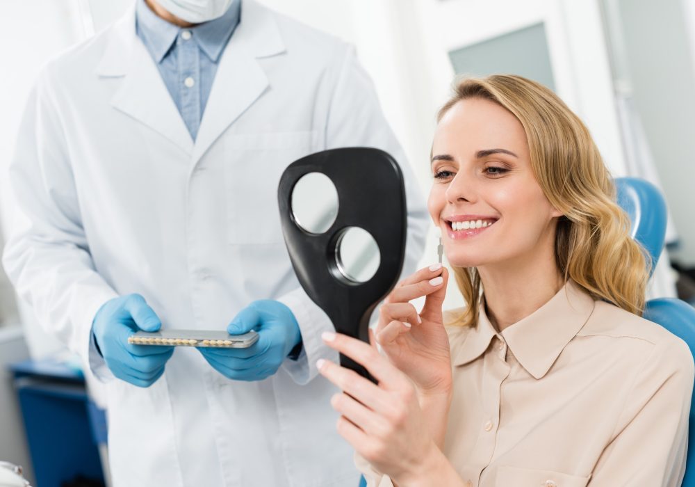 woman-choosing-tooth-implant-looking-at-mirror-in-modern-dental-clinic.jpg
